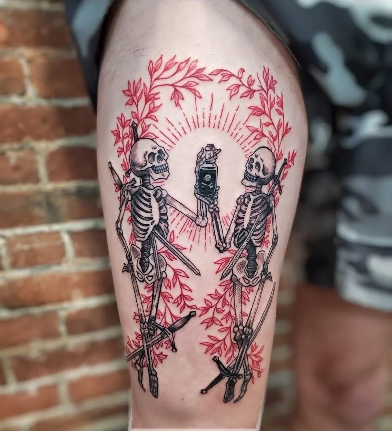 Tattoo of two skeletons with swords, holding a flip phone, surrounded by red leaves, with radiant lines behind them.