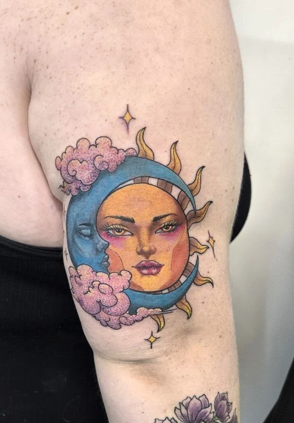 Tattoo of a sun and moon with a woman's face in the center, surrounded by clouds and stars on upper arm