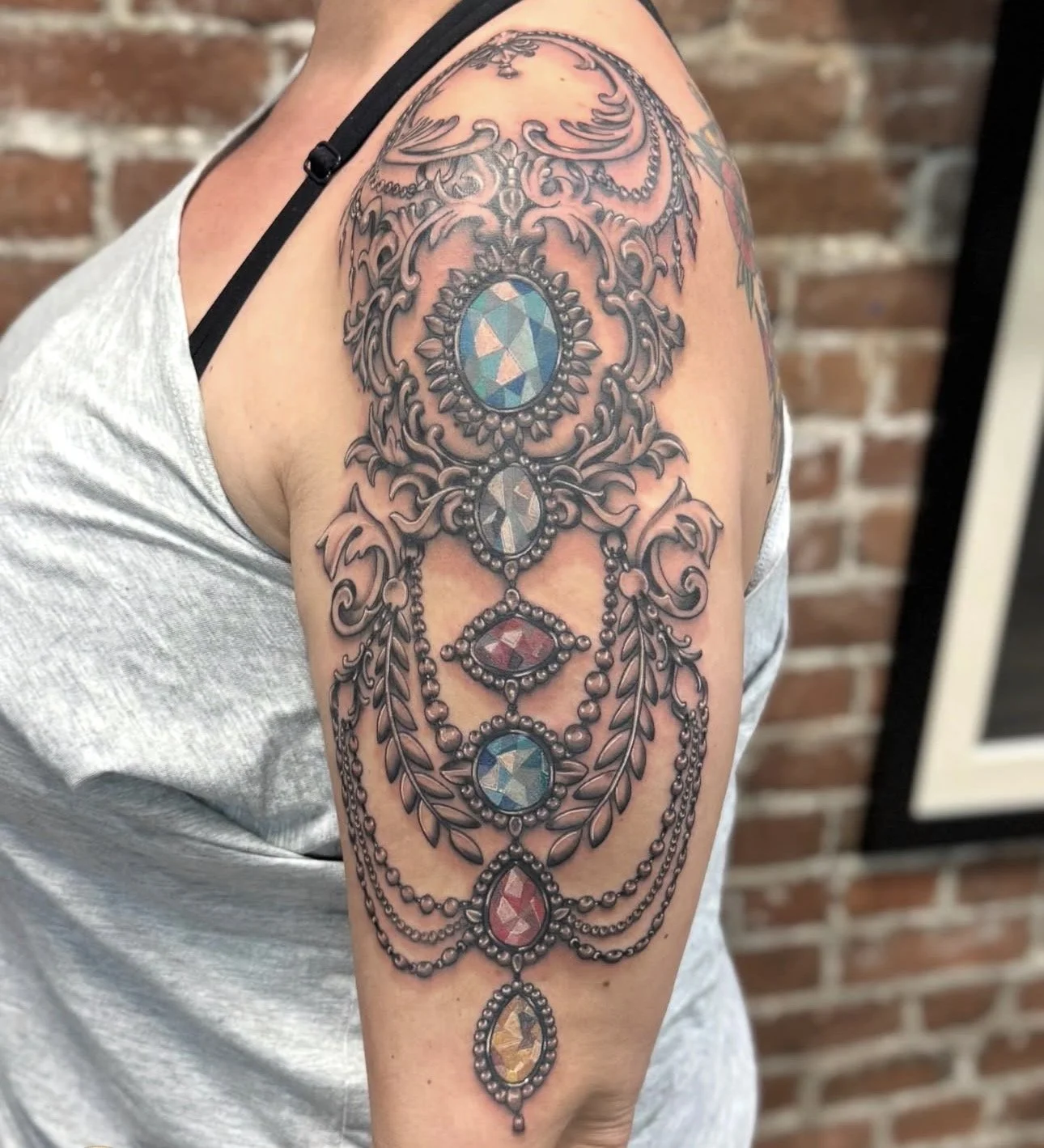 Colorful tattoo of a chandelier with gemstones and intricate details on a person's upper arm.