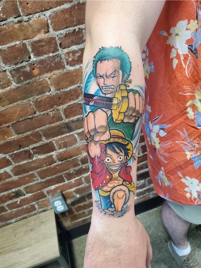 Colorful tattoo on person's forearm featuring characters from One Piece, Luffy and Zoro, with vibrant colors and detailed line work.