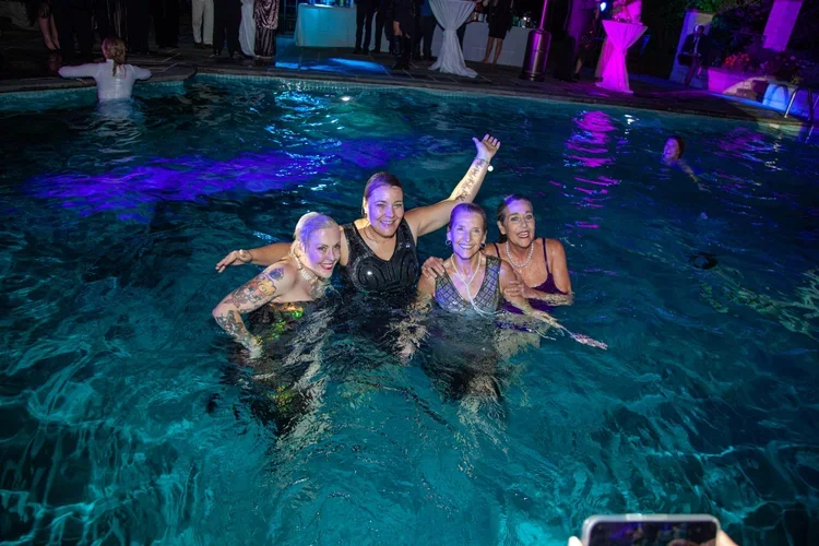 Four women, with colorful party lights and other guests in the background.