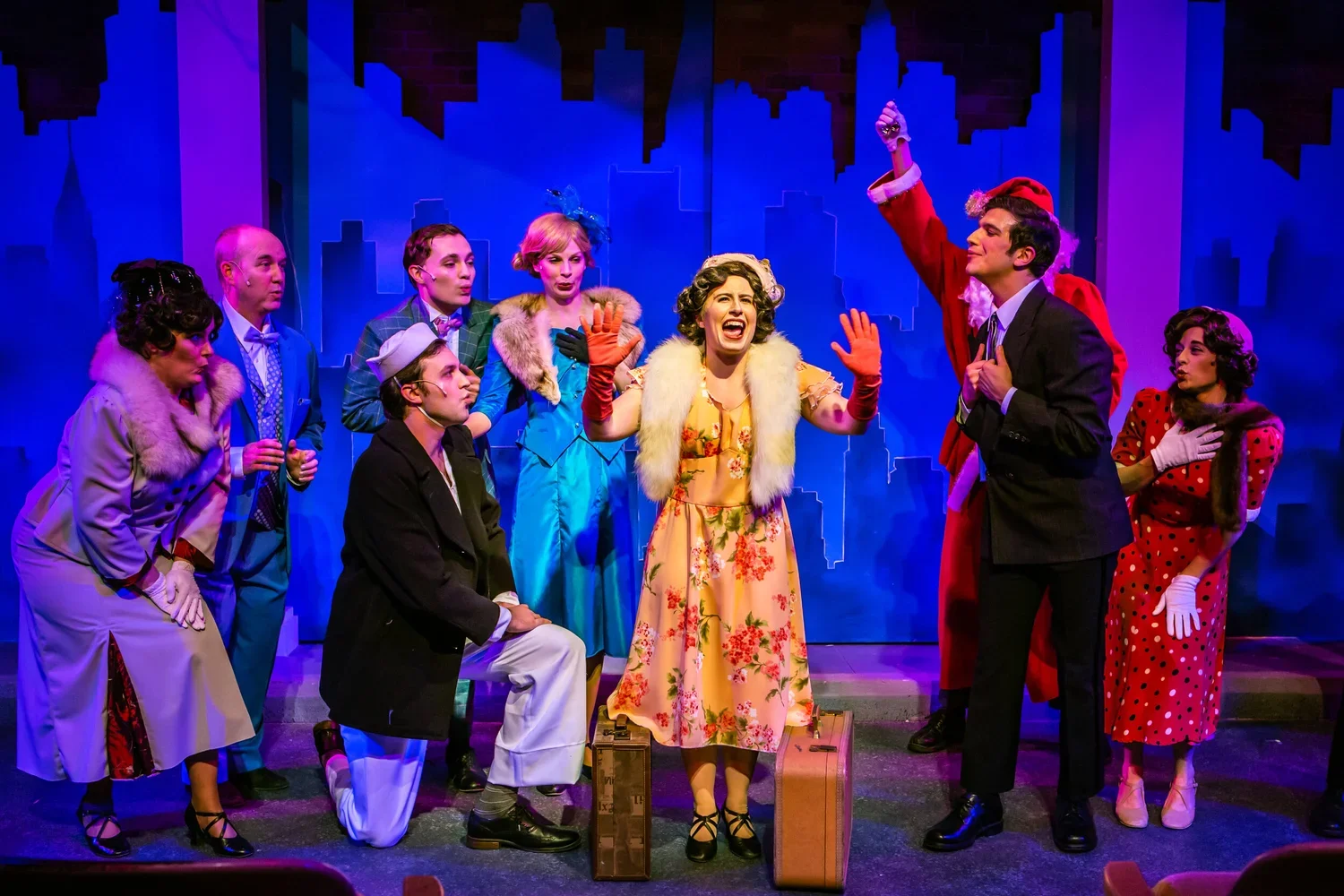 A theatrical stage scene with actors in vintage clothing, colorful costumes, and expressive poses, suggesting a lively musical performance.