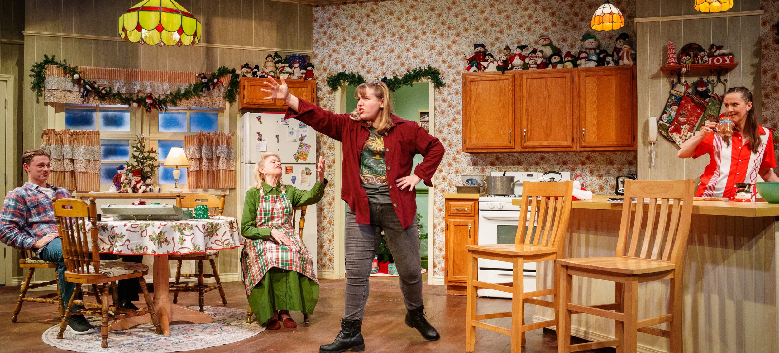 A group of four people performing a Citadel's Miracle on South Division Street play in a decorated kitchen set, with decorations of snowmen and Christmas stockings.
