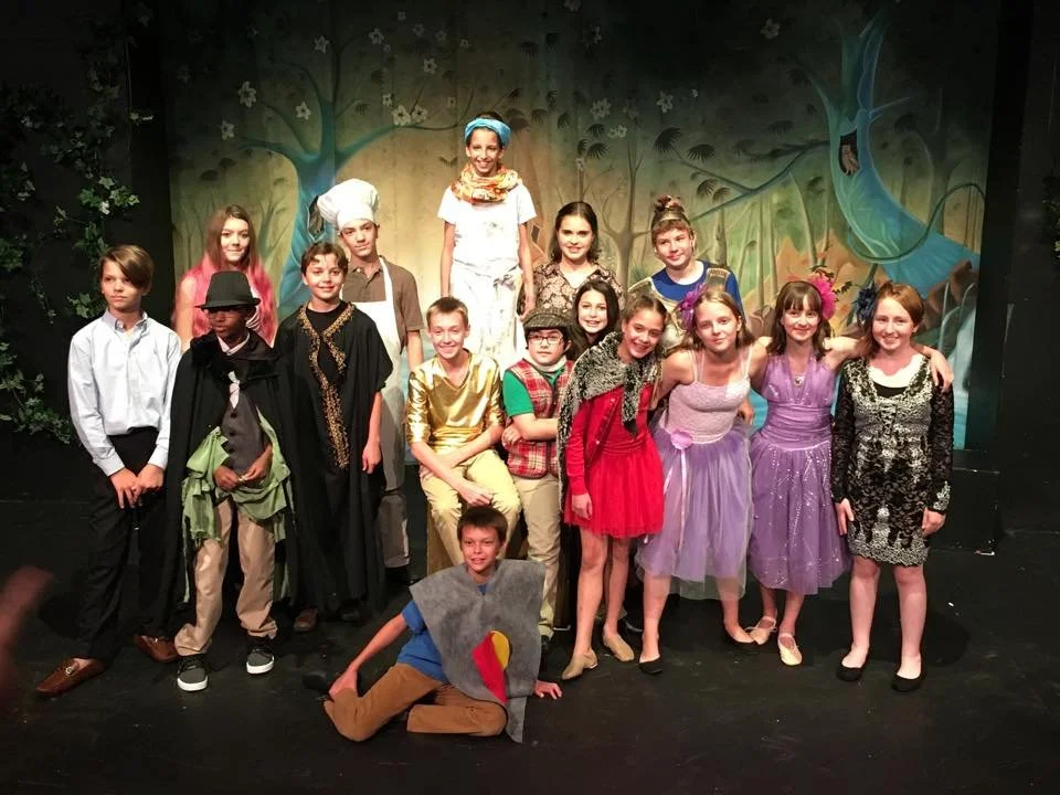 Kids from Citadel's Youth Education Program dressed in costumes for a theater play, standing on stage with a painted forest backdrop.