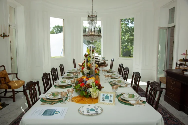 A long dining table at Citadel's 12th Annual Gala is set with floral centerpieces, plates, glasses, and napkins in a bright room with large windows and a chandelier.
