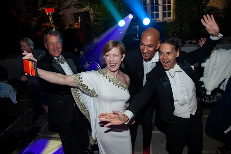 People dressed in formal attire dancing and taking selfies at a party with colorful lights.