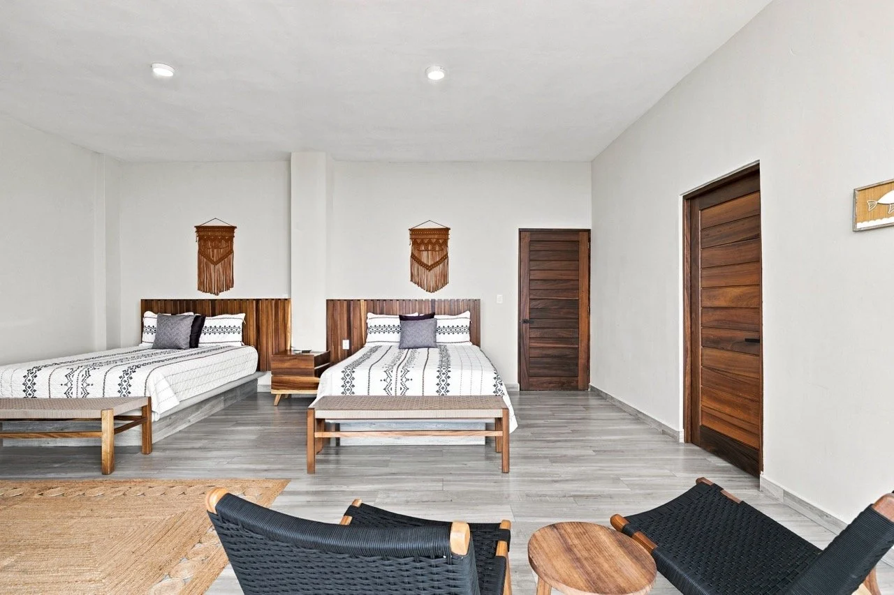 Habitación con dos camas, paredes blancas, puertas de madera y decoraciones de telar artesanal