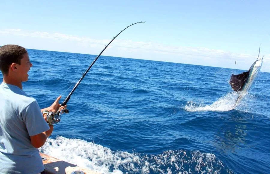 Joven pescando en el océano mientras un pez salta del agua.