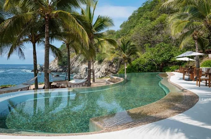 Piscina infinita en un resort junto a la playa con palmeras y vistas al mar
