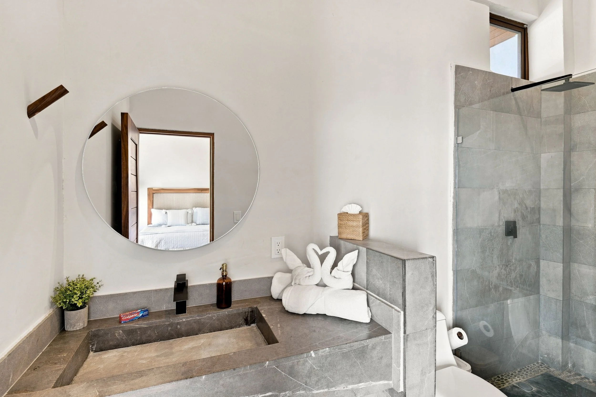 Baño moderno con ducha abierta, inodoro y accesorios decorativos en tonos neutros, incluyendo toallas enrolladas con forma de cisnes.