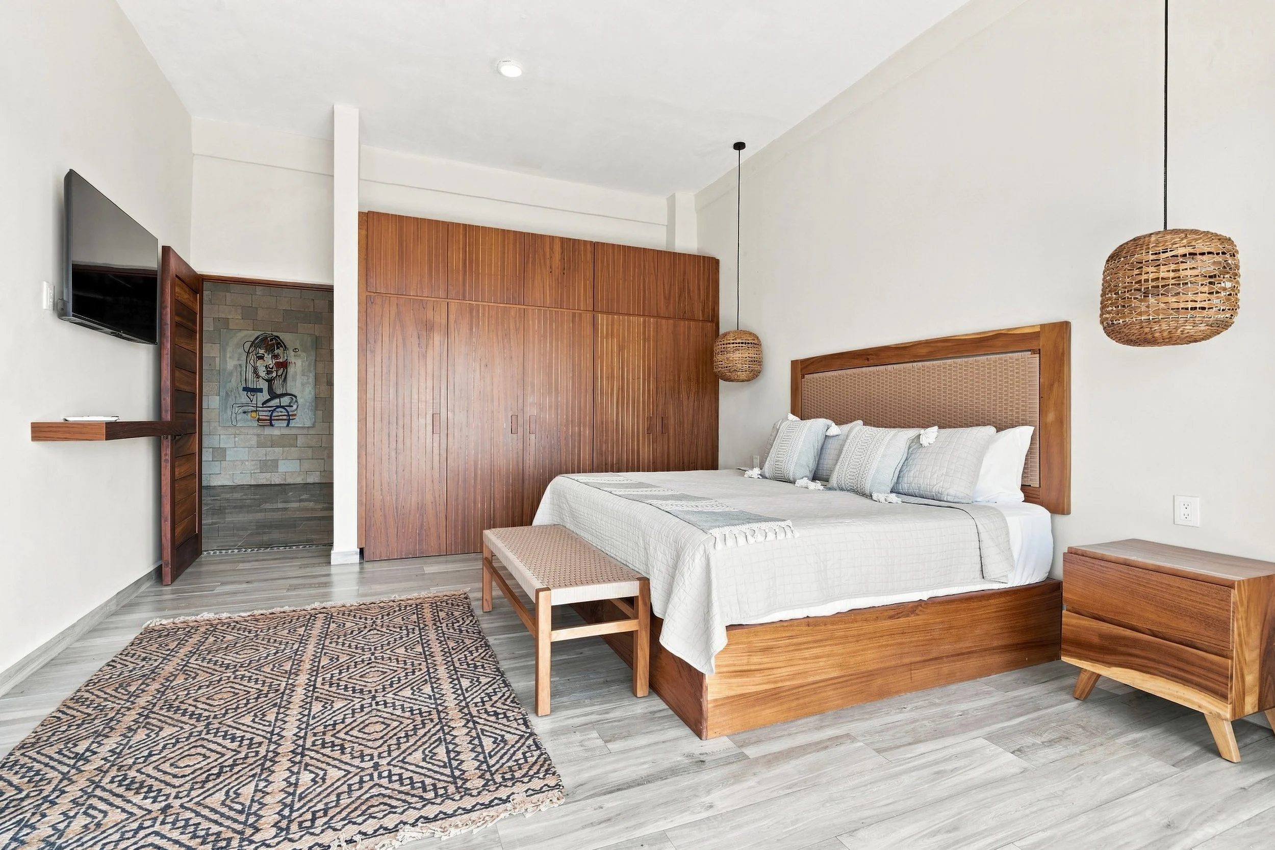 Habitación moderna con cama, cabecera de madera, lamparitas de mimbre colgantes, armario de madera y un televisor en la pared