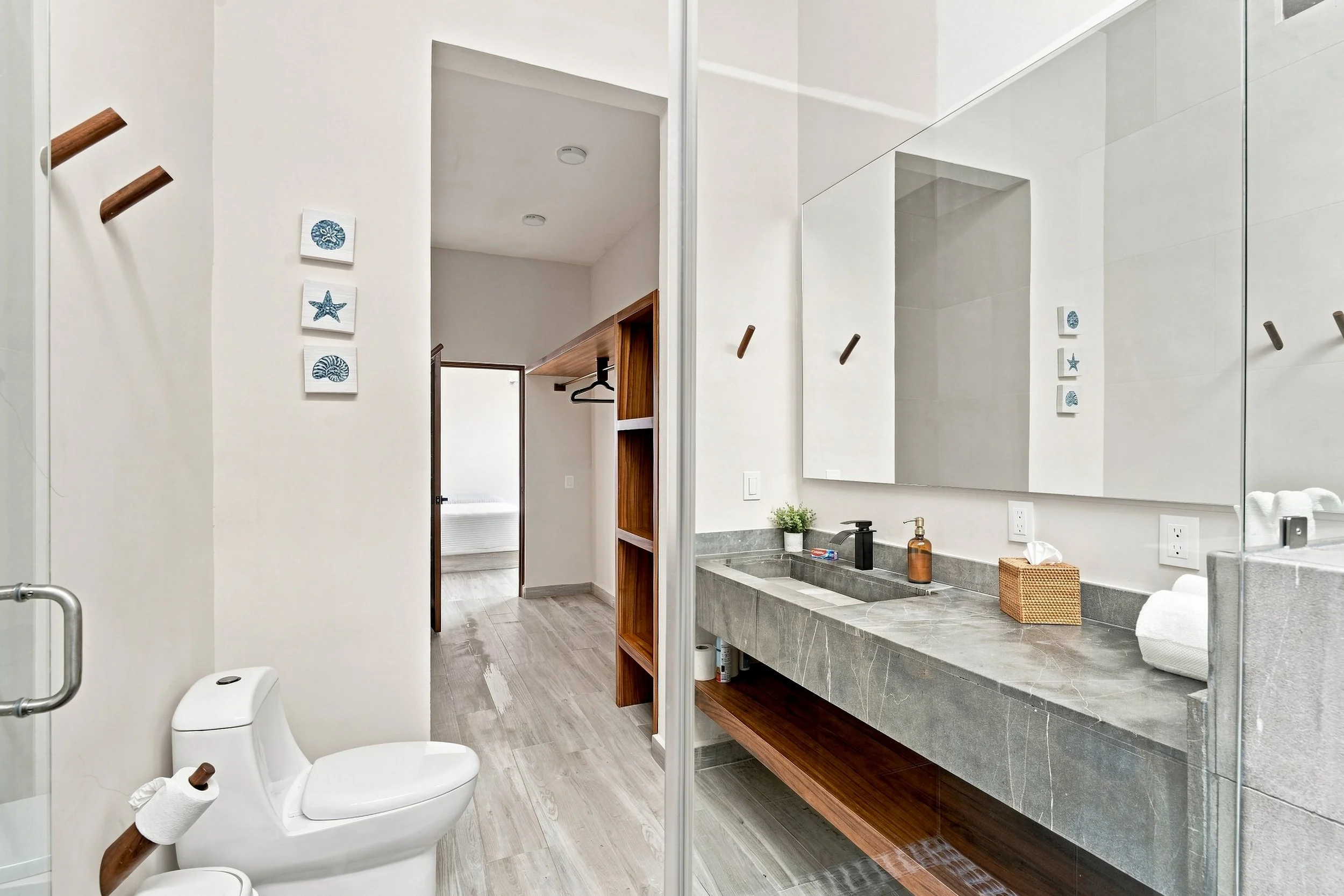 Baño moderno con inodoro, lavabo con espejo grande, gabinetes de madera, y decoraciones en la pared estilo marino.