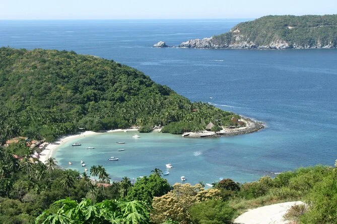 Vista panorámica de una ensenada en una región montañosa con agua azul, rodeada de vegetación tropical, con varias embarcaciones descansando en la playa y en el agua.