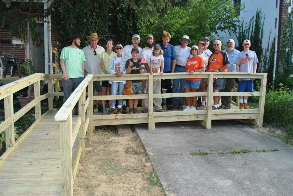 Group of people, including children and adults, standing behind a newly constructed wooden ramp outside in a garden or backyard.