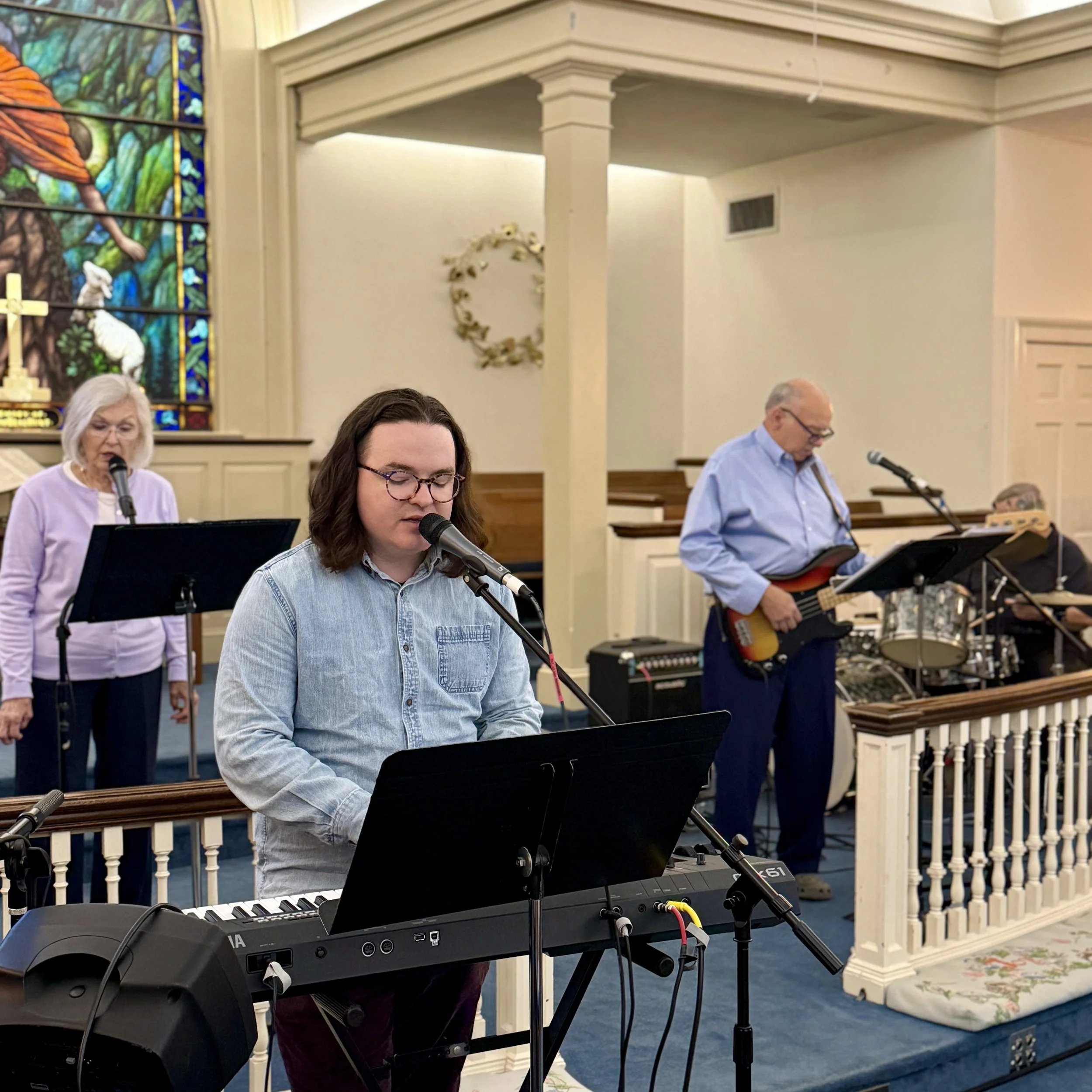 People playing musical instruments and singing in a church with stained glass windows and church decor.