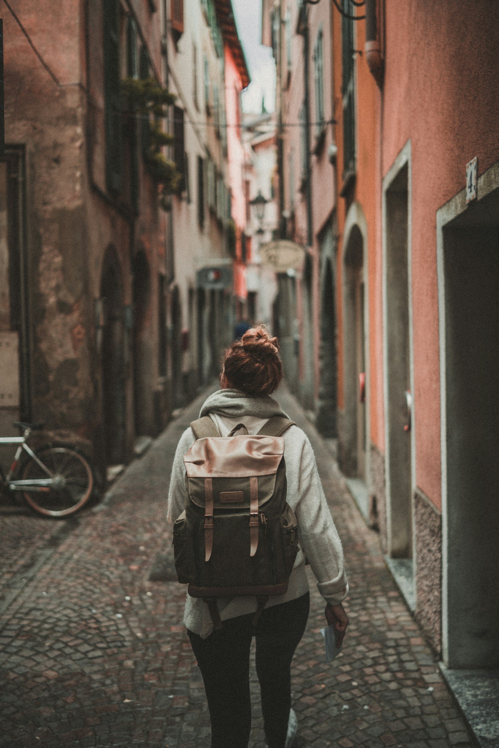 A person with a backpack walking down a narrow cobblestone street lined with colorful apartment buildings.