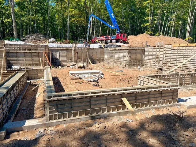 Construction site with foundation forms and a crane with a boom in wooded area.