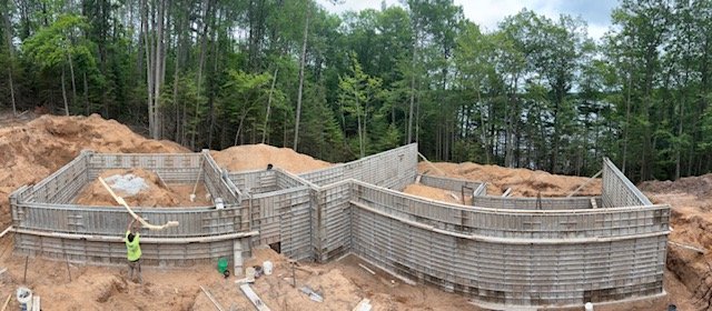 Construction site with wooden forms for a concrete wall, workers, and trees in the background.