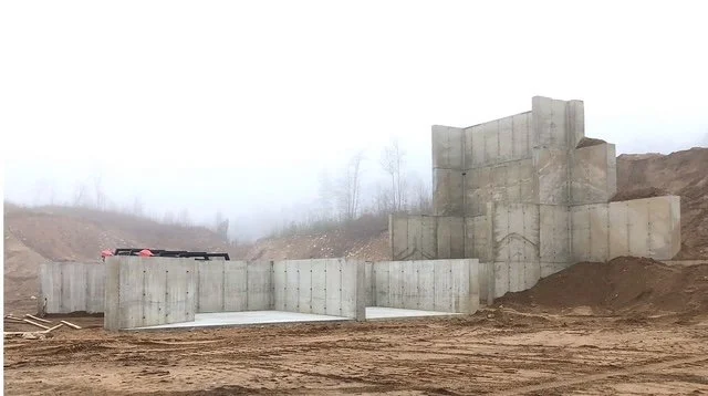 Construction site with concrete retaining wall or structure on a dirt slope, foggy background with some trees.