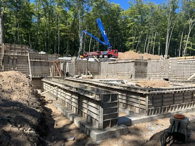 Construction site with concrete formwork and a blue crane, surrounded by trees.