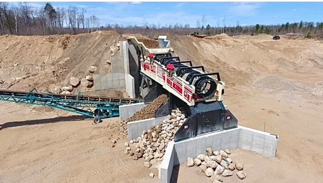 Large construction machine crushing rocks at a quarry site with a conveyor belt transporting debris.