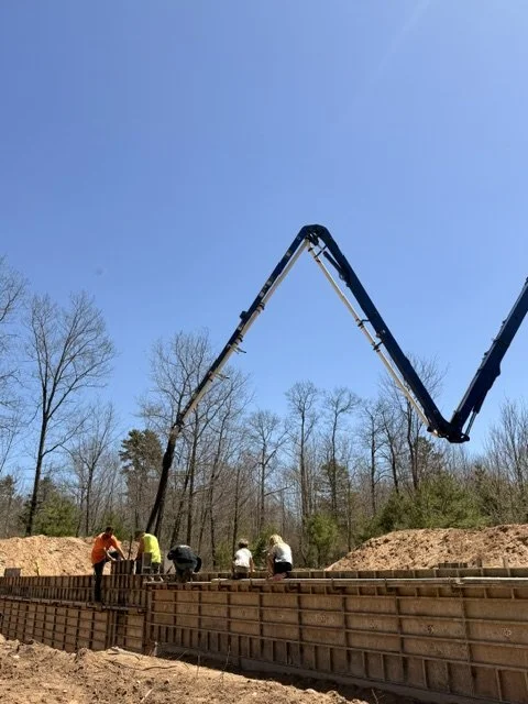 Construction workers at a building site with a concrete foundation and a cement pump truck pouring concrete.