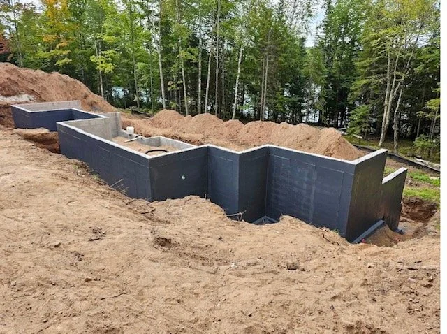 Construction of a basement foundation with concrete walls on a sloped site surrounded by trees.