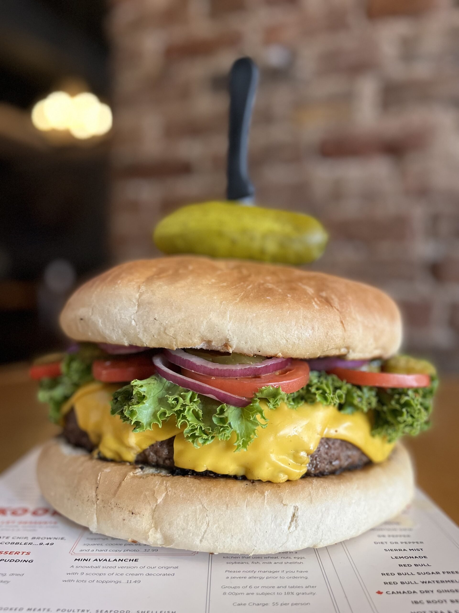 Close-up view of a cheeseburger with lettuce, tomato, red onion, pickles, melted cheese, and a beef patty in a bun.