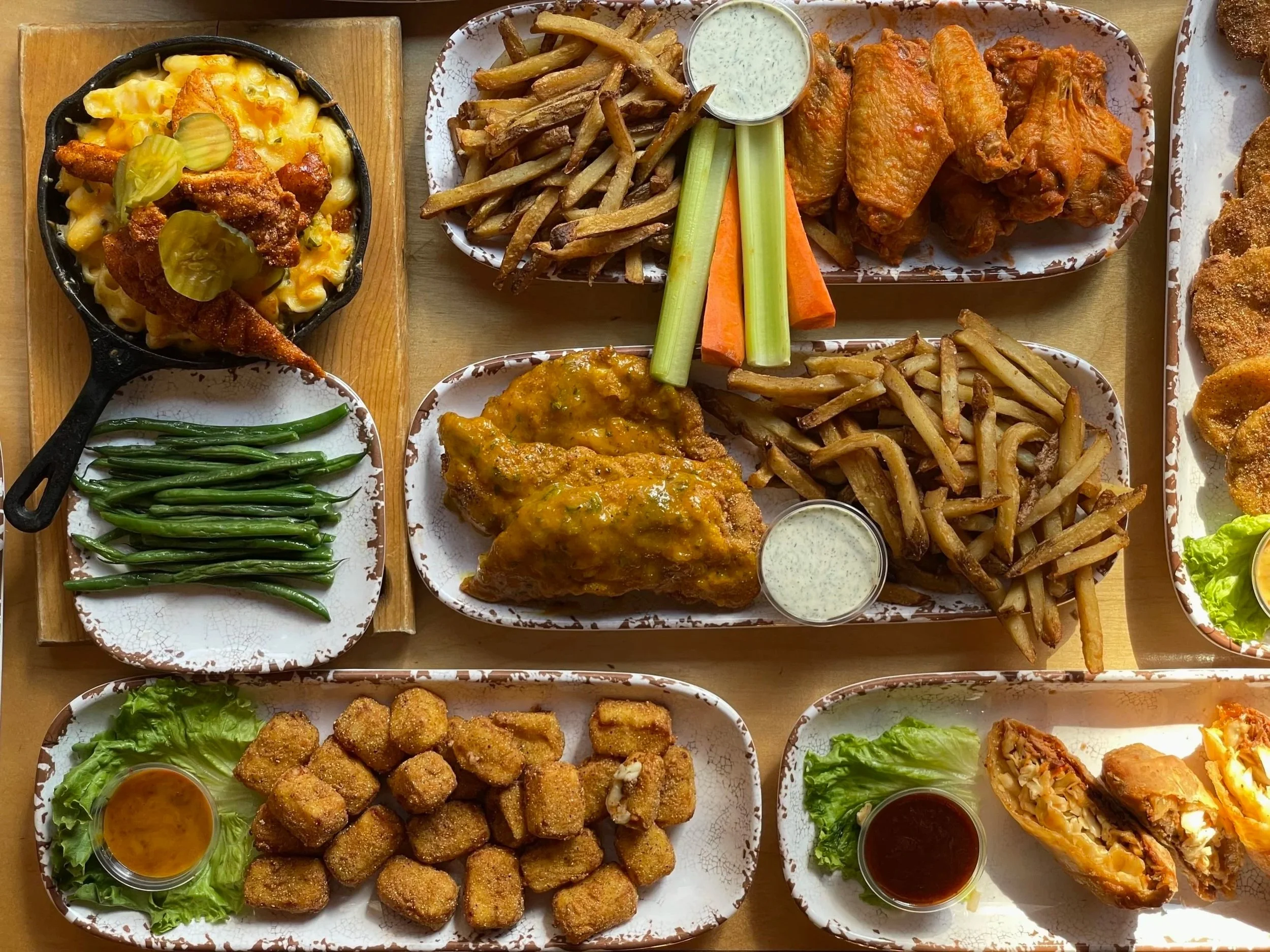Assorted plates of fried foods including chicken wings, French fries, fried fish, breaded chicken nuggets, and egg rolls, with dipping sauces and garnishes.