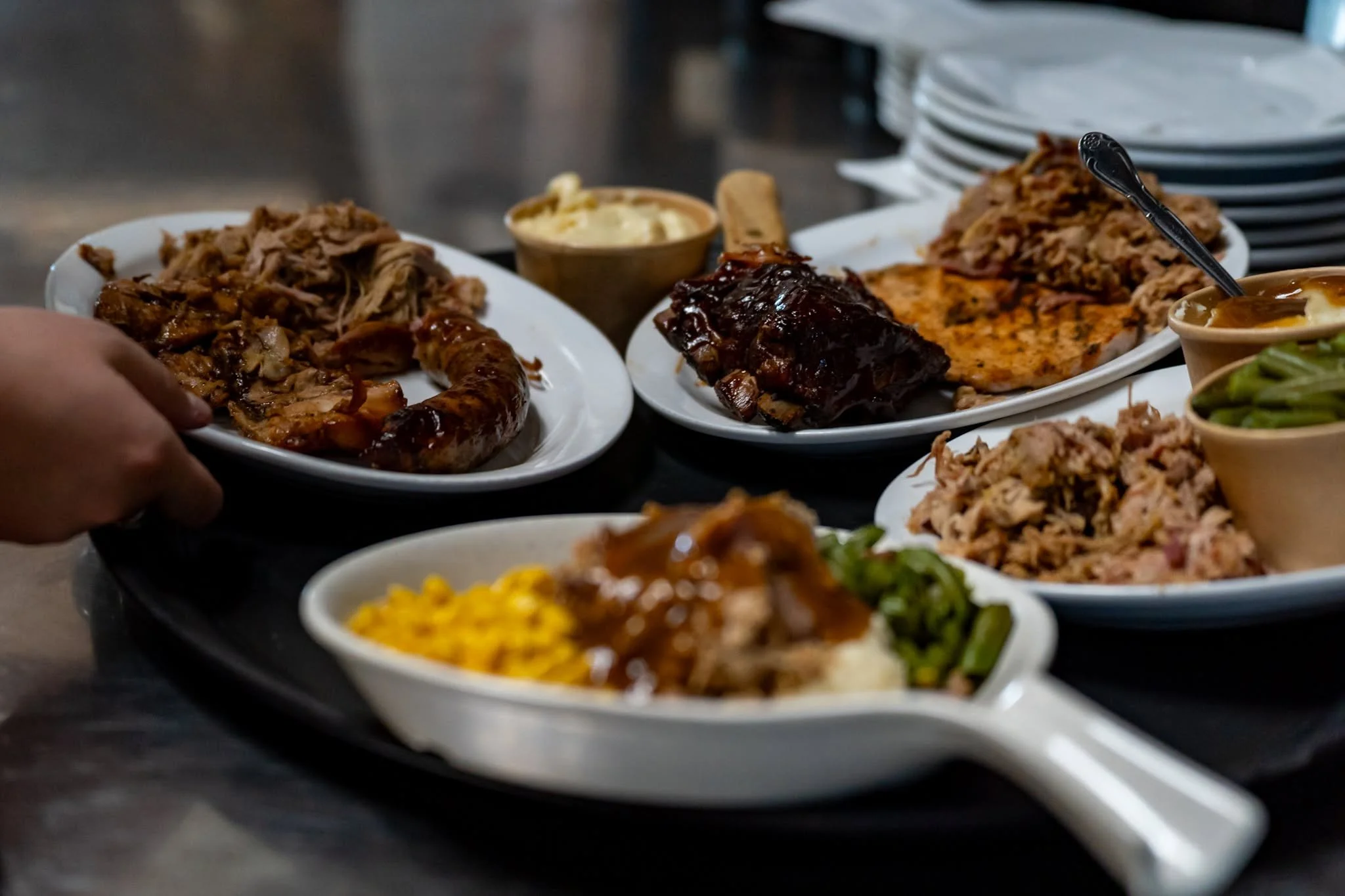 Assorted dishes of barbecue, sides, and sauces on white plates at a restaurant table.