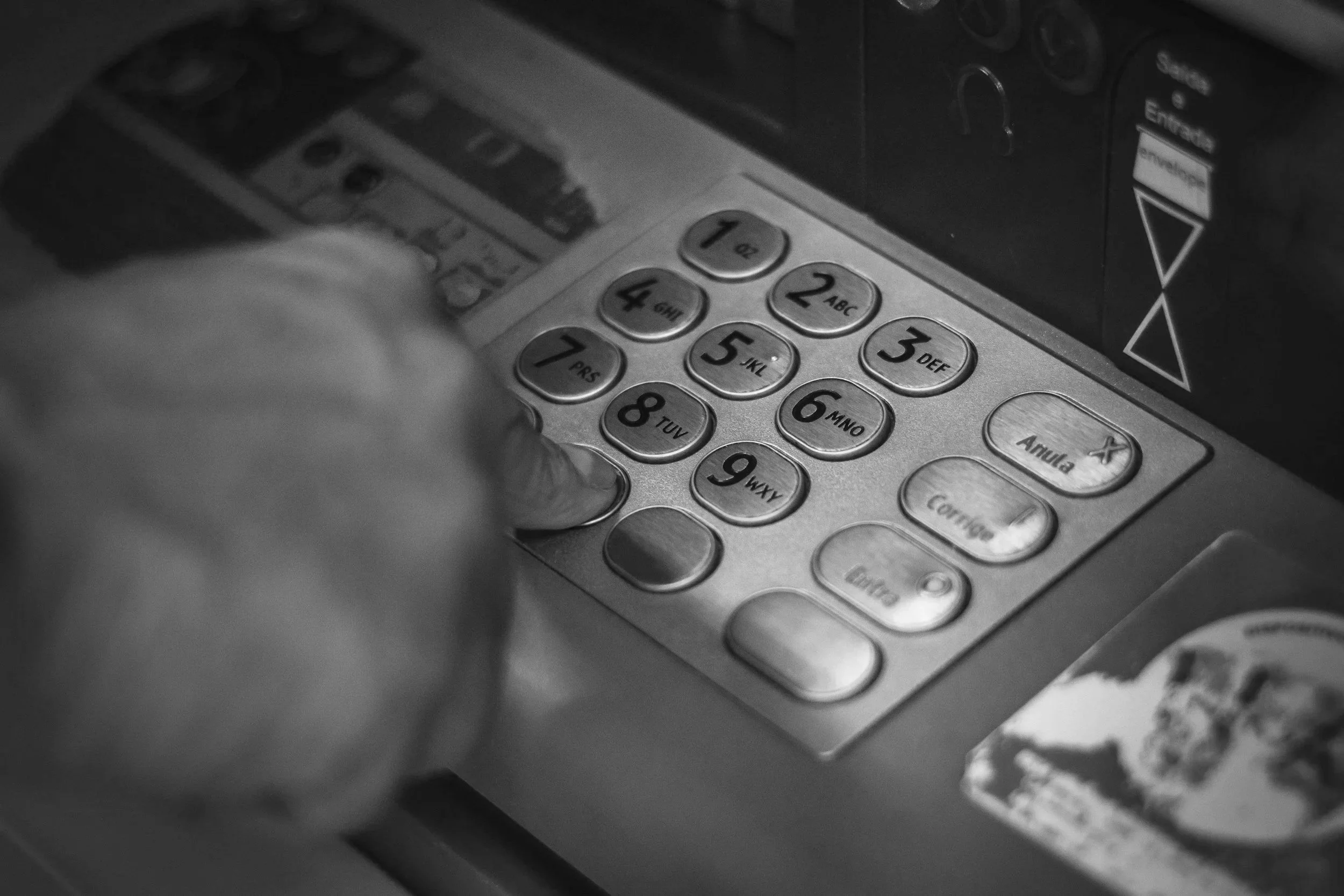 Black and white close-up photo of a keypad on an ATM machine with a hand pressing the number 7 key.