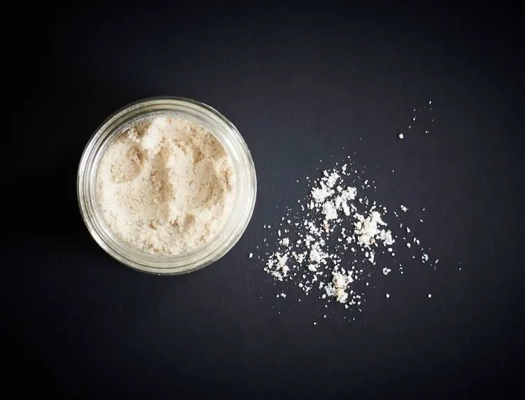 A white powdered mahleb in a bowl and sprinkled on a black background