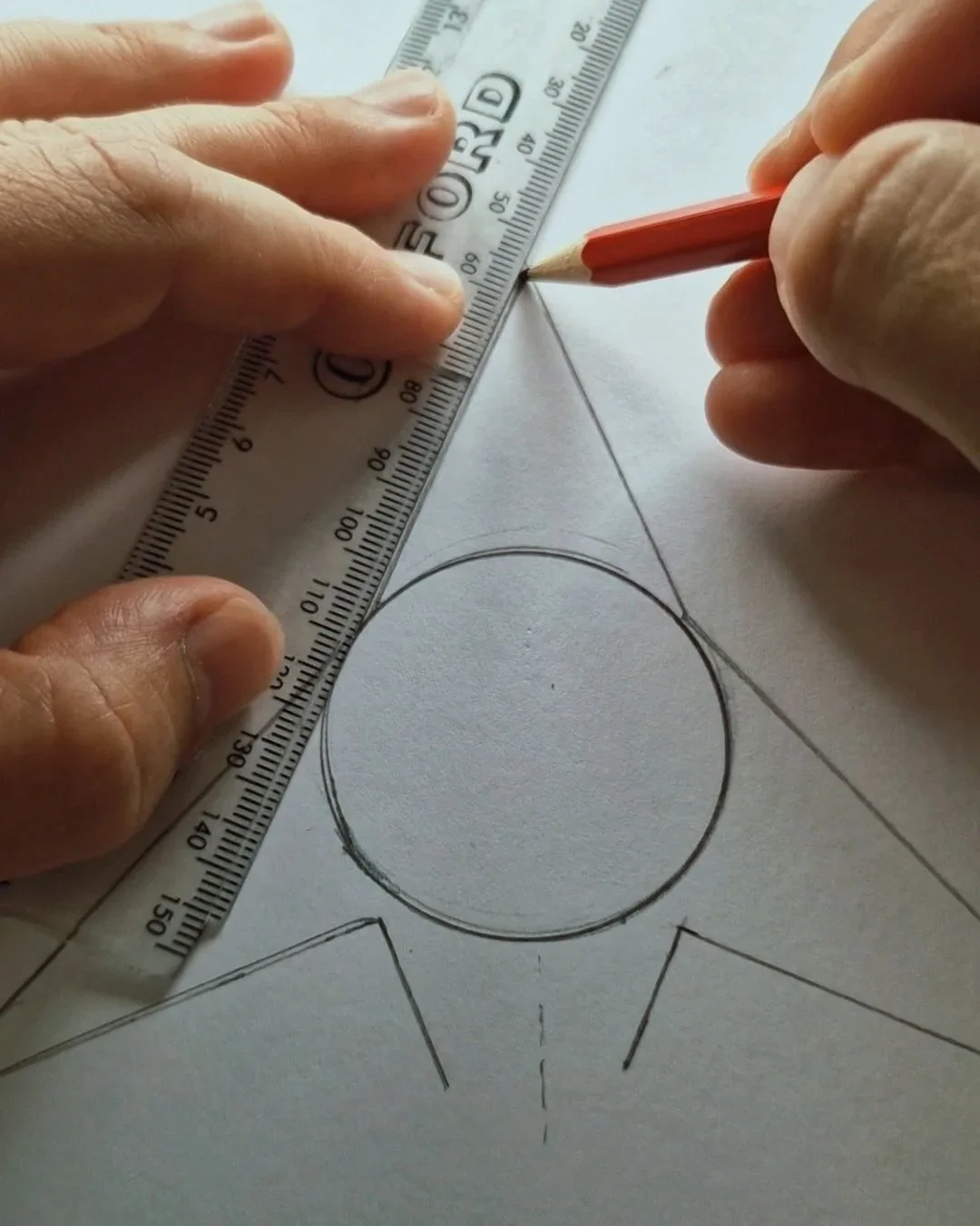 A person is drawing a geometric design with a pencil and a ruler on white paper, which includes circles and lines, possibly for an art or technical project.