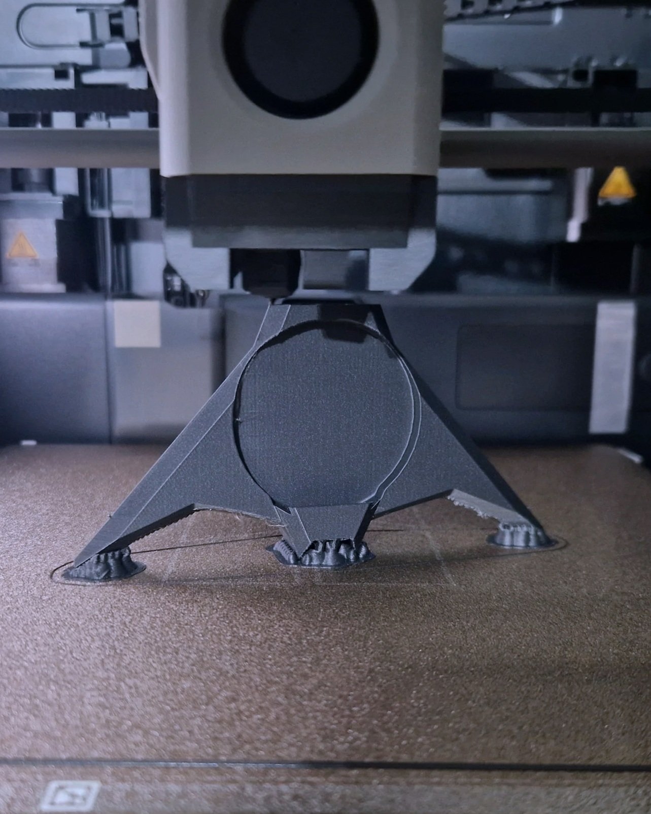 Close-up of a metal stand with three legs supporting a piece of equipment, with a circular object mounted on top. The stand is placed on a brown carpeted floor.