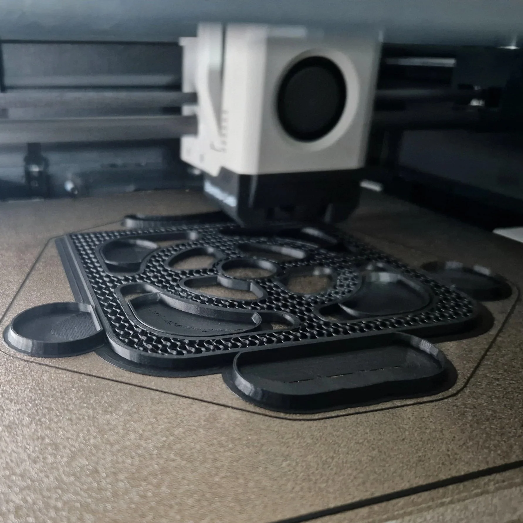 Close-up of a black silicone mold with various oval and circular cavities, placed on a beige countertop. Part of a kitchen stovetop is visible in the background.