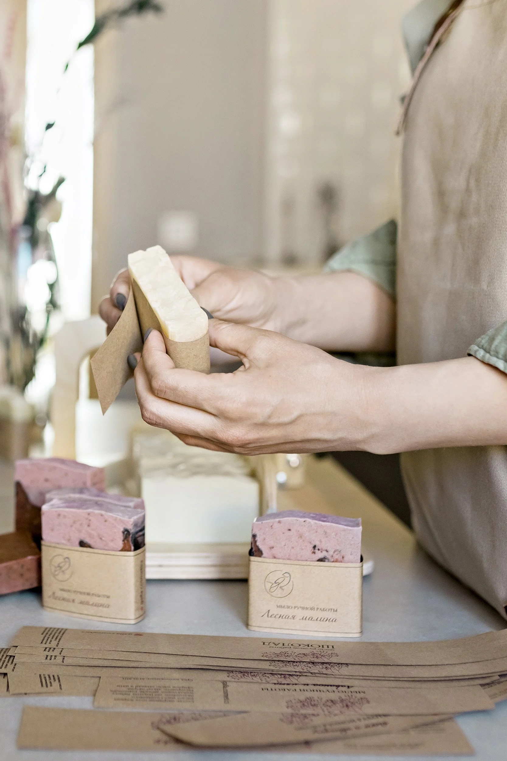 Person holding a soap bar, with soap bars and folded paper documents on the table in front of them.