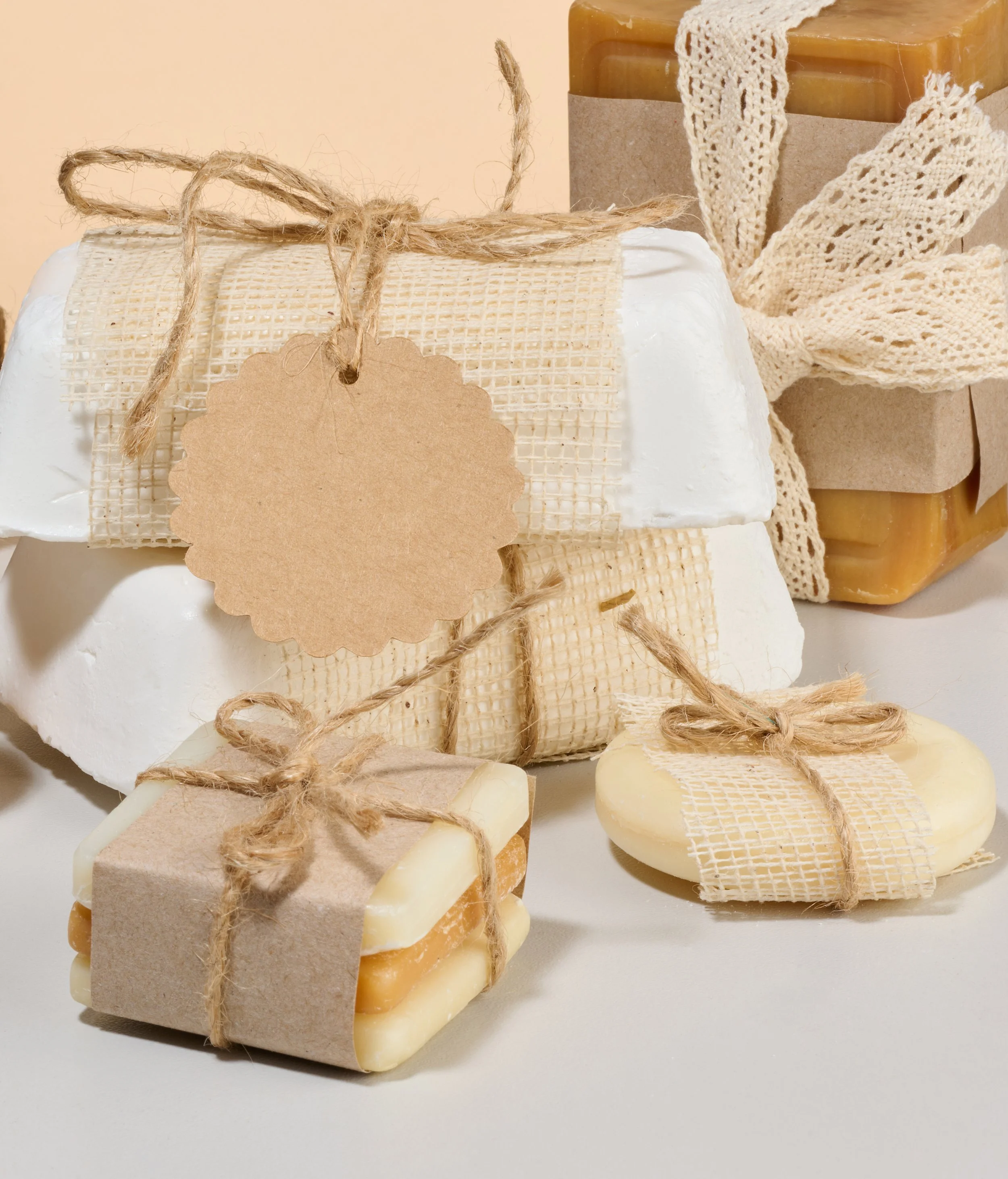 Several handmade soap bars wrapped with twine and kraft paper, some topped with honey-colored soap, arranged on a white surface.