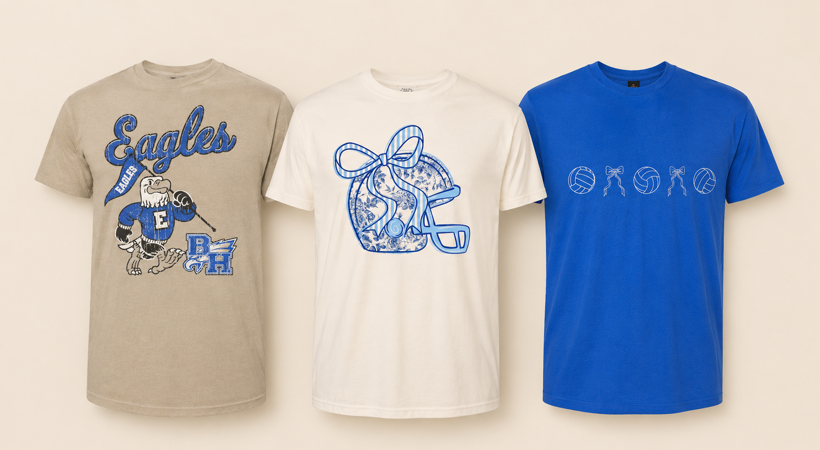 Three T-shirts hanging on a wall, featuring sports and graphic designs. The left shirt is beige with a blue and white eagle mascot holding a golf club, with the words 'Eagles' and additional letters 'B' and 'H'. The middle shirt is white with a large outline of a gift box decorated with floral patterns and a big bow, with a letter 'A'. The right shirt is blue with a line of volleyballs and bows connecting them across the chest.