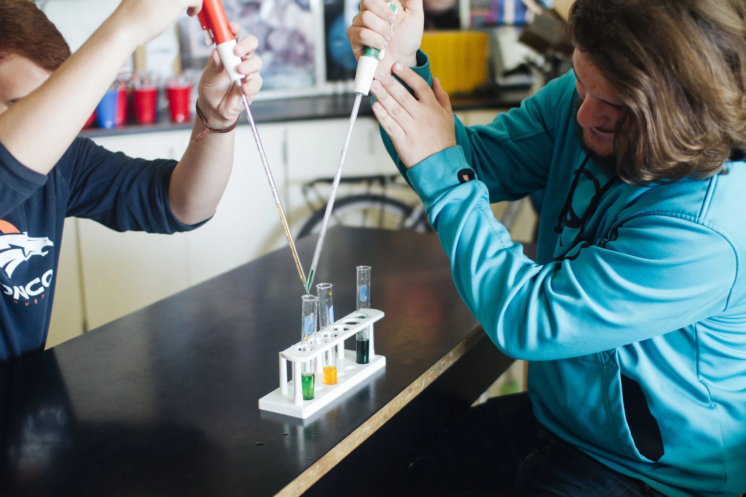 Two Columbia Falls students conducting a science experiment with test tubes and pipettes in a laboratory or classroom setting.