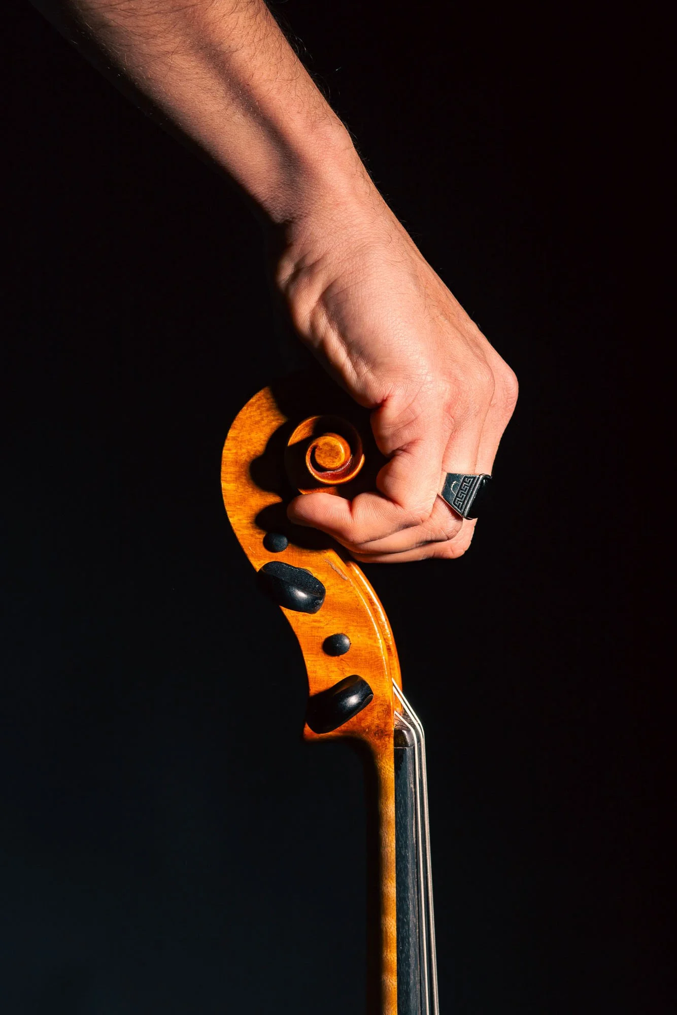 Mano che tiene con forza l’archetto di un violino, visibile solo parzialmente, contro uno sfondo nero.