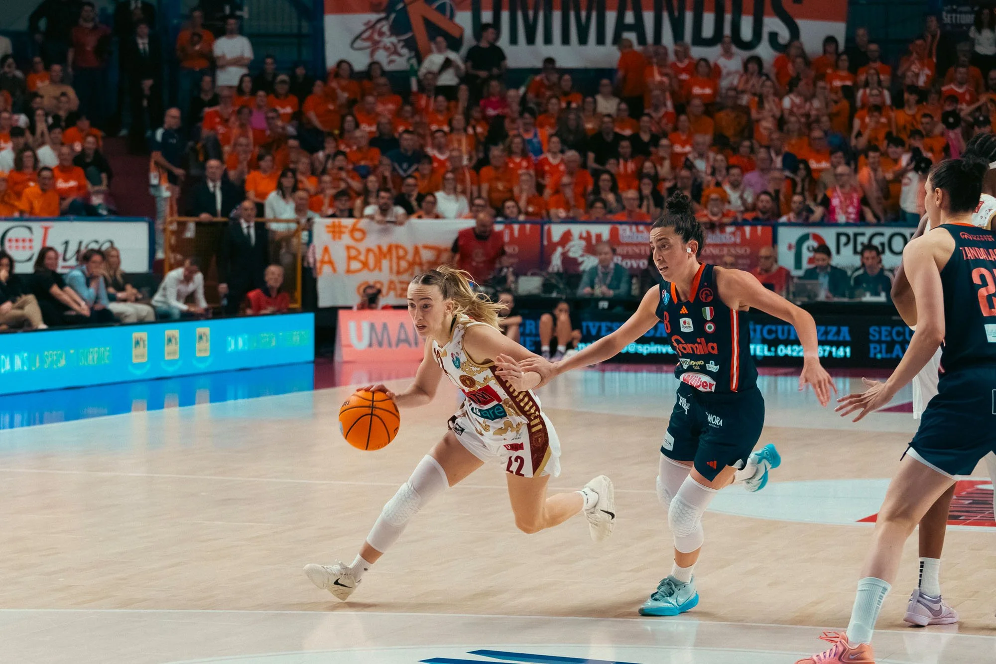 Partita di pallacanestro tra due squadre di donne con pubblico sugli spalti
