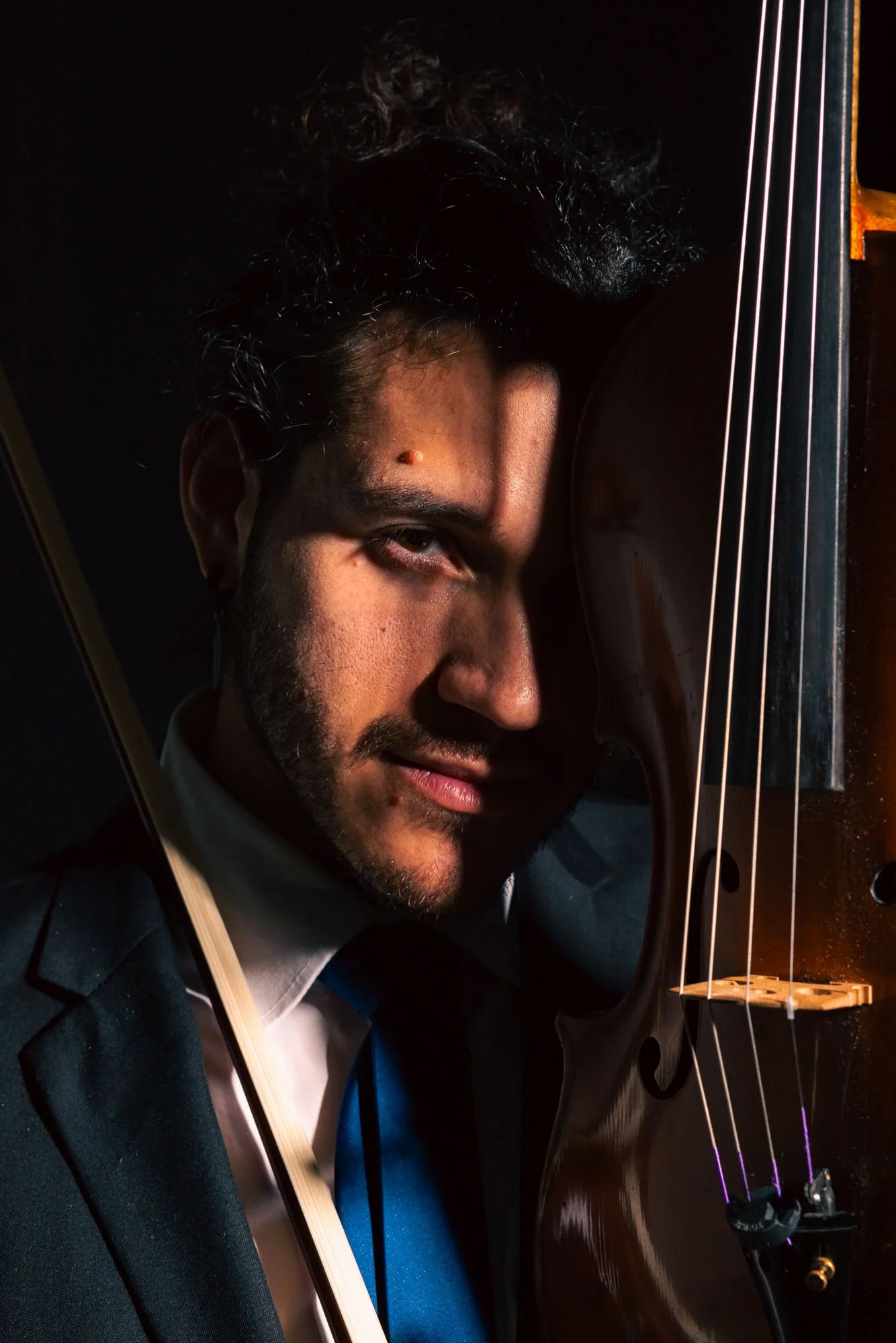 Uomo con barba, capelli ricci e scarsamente visibile, che suona il violino in un'ambientazione scura