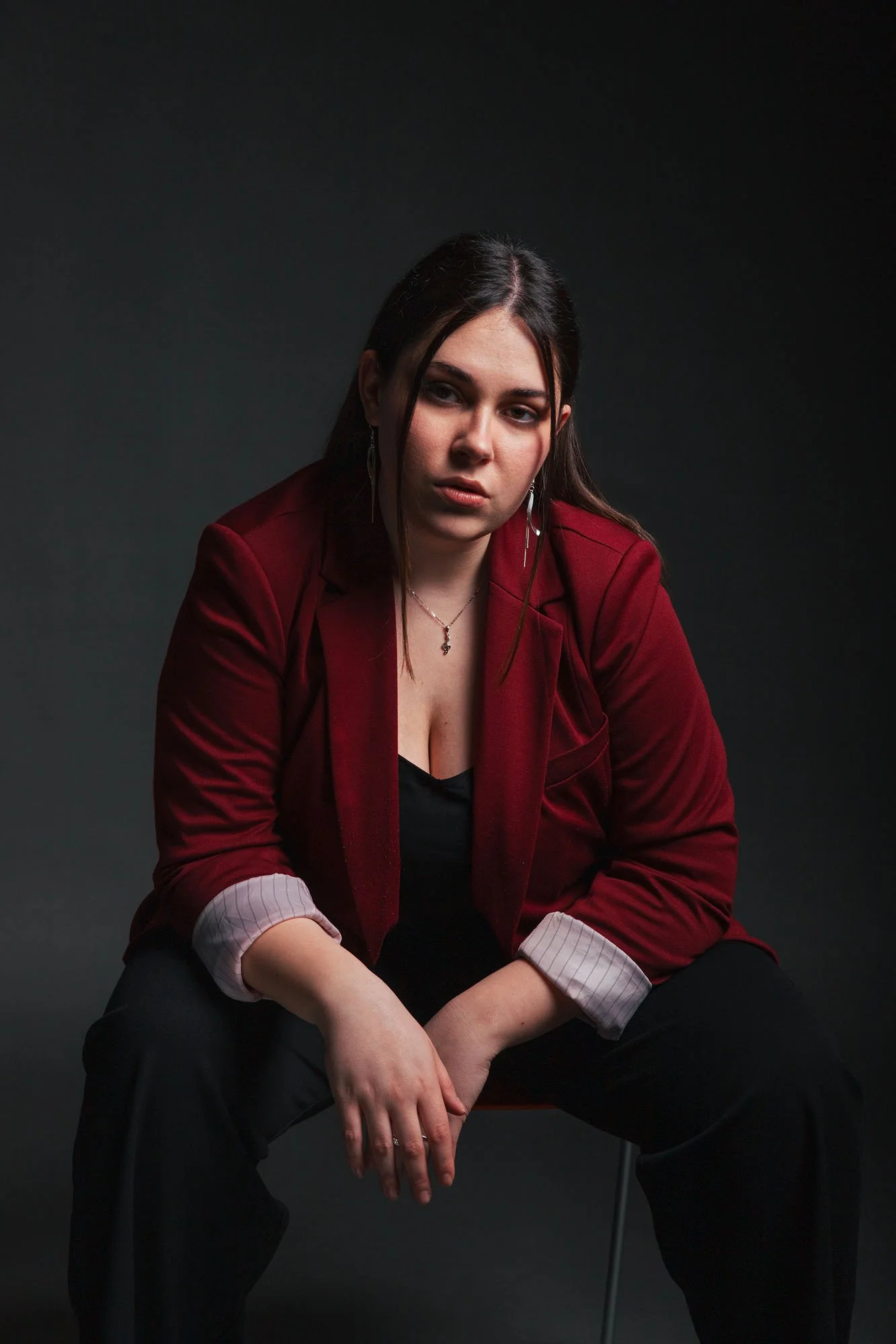 Ragazza seduta con abbigliamento elegante rossa e nera, sfondo scuro.