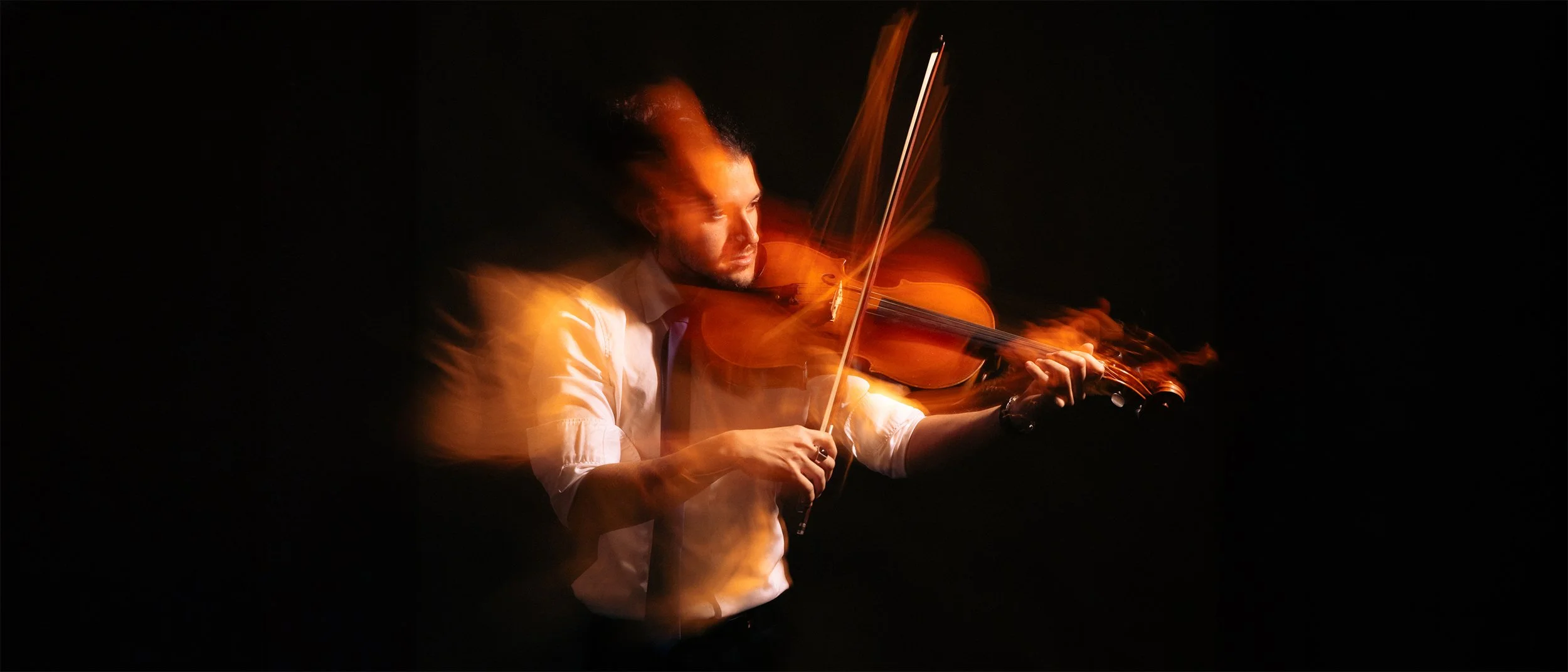 Uomo che suona un violino in un ambiente scuro con effetti di luci calde e movimento.