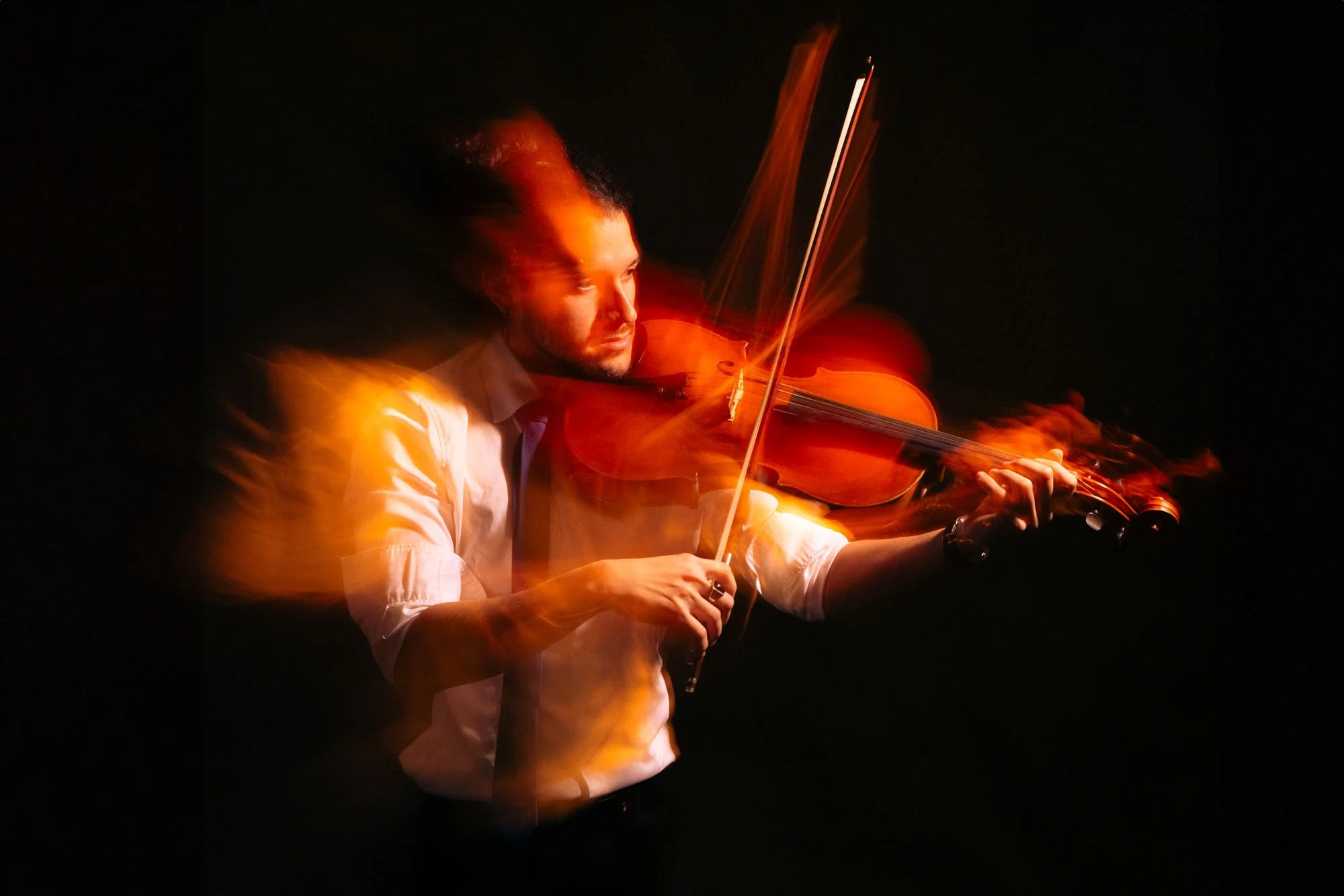 Una persona suona il violino in uno spazio buio, con effetti di luce calda che creano un'atmosfera intensa.
