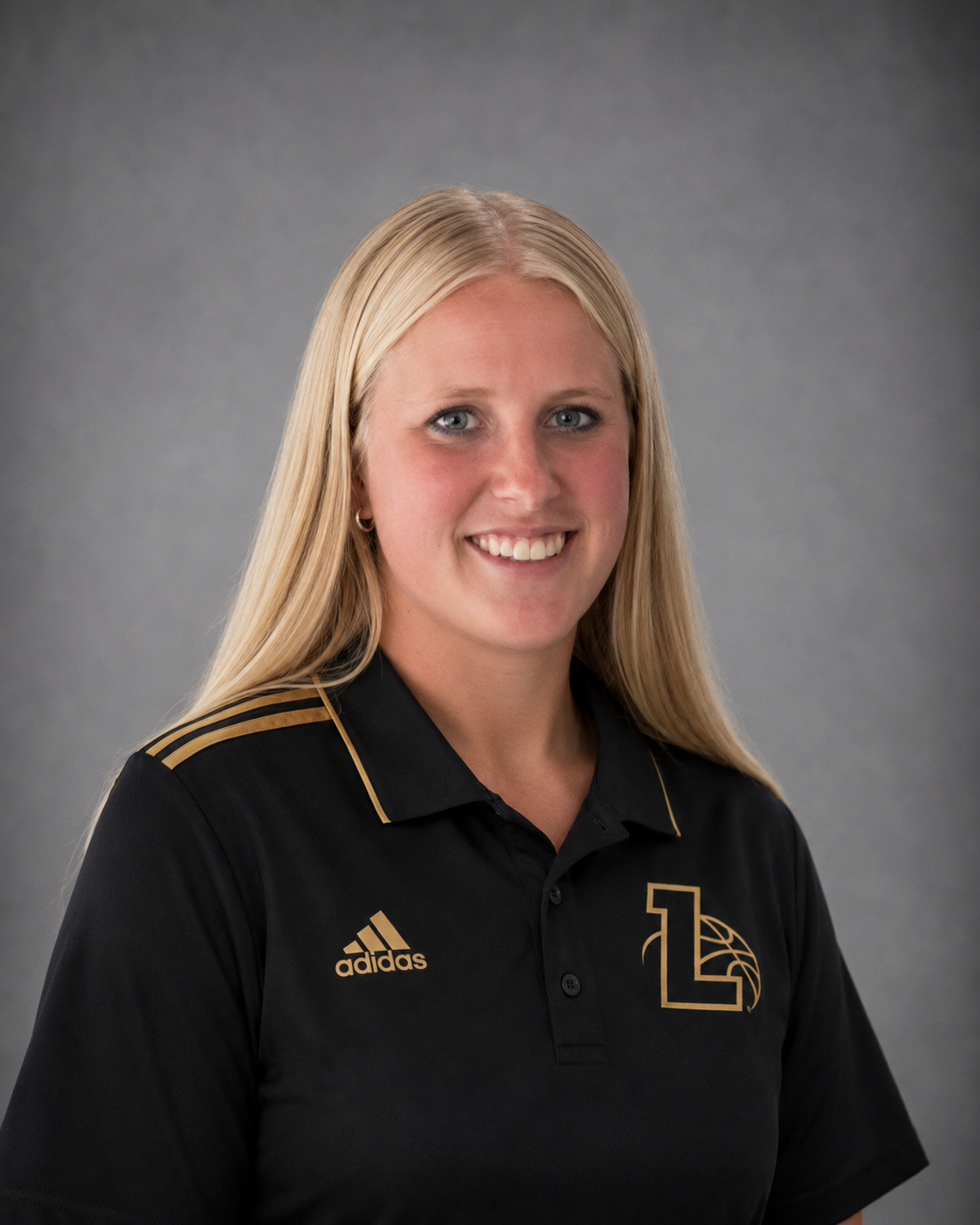 Professional woman with long blonde hair smiling at the camera, wearing a black Adidas polo shirt with gold accents and a logo with the letter L and a basketball design.