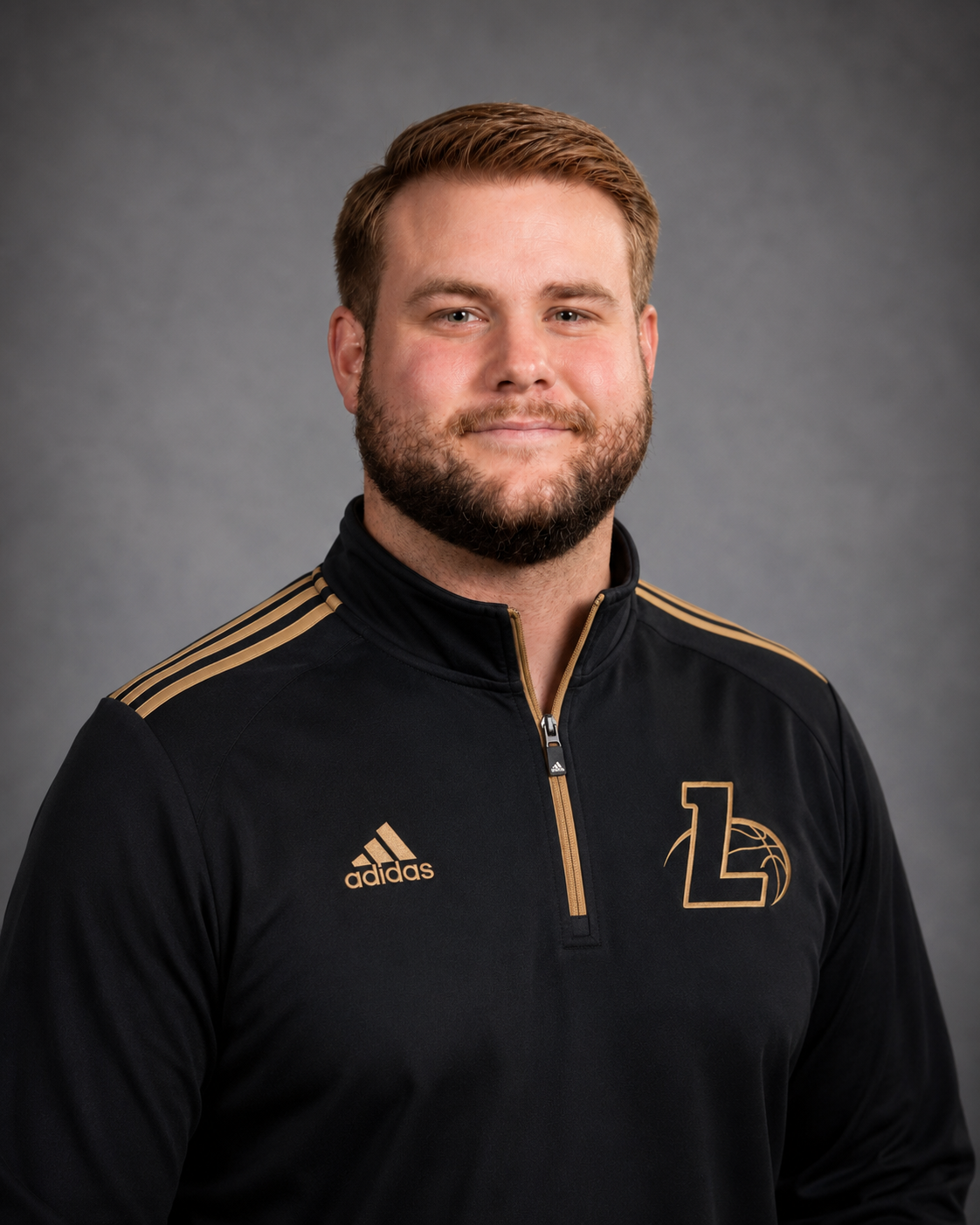 Headshot of a man with short red hair and a beard, wearing a black Adidas sports jacket with gold accents and a logo featuring a number 1 and a basketball.