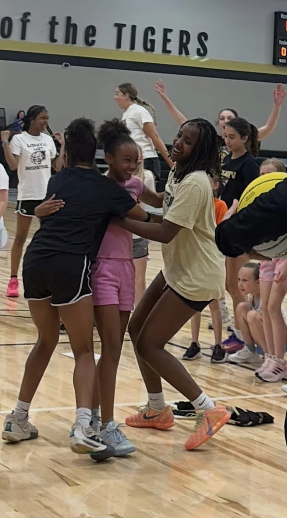 Young girls playing and having fun at a gym or sports practice, celebrating with hugs and smiles.