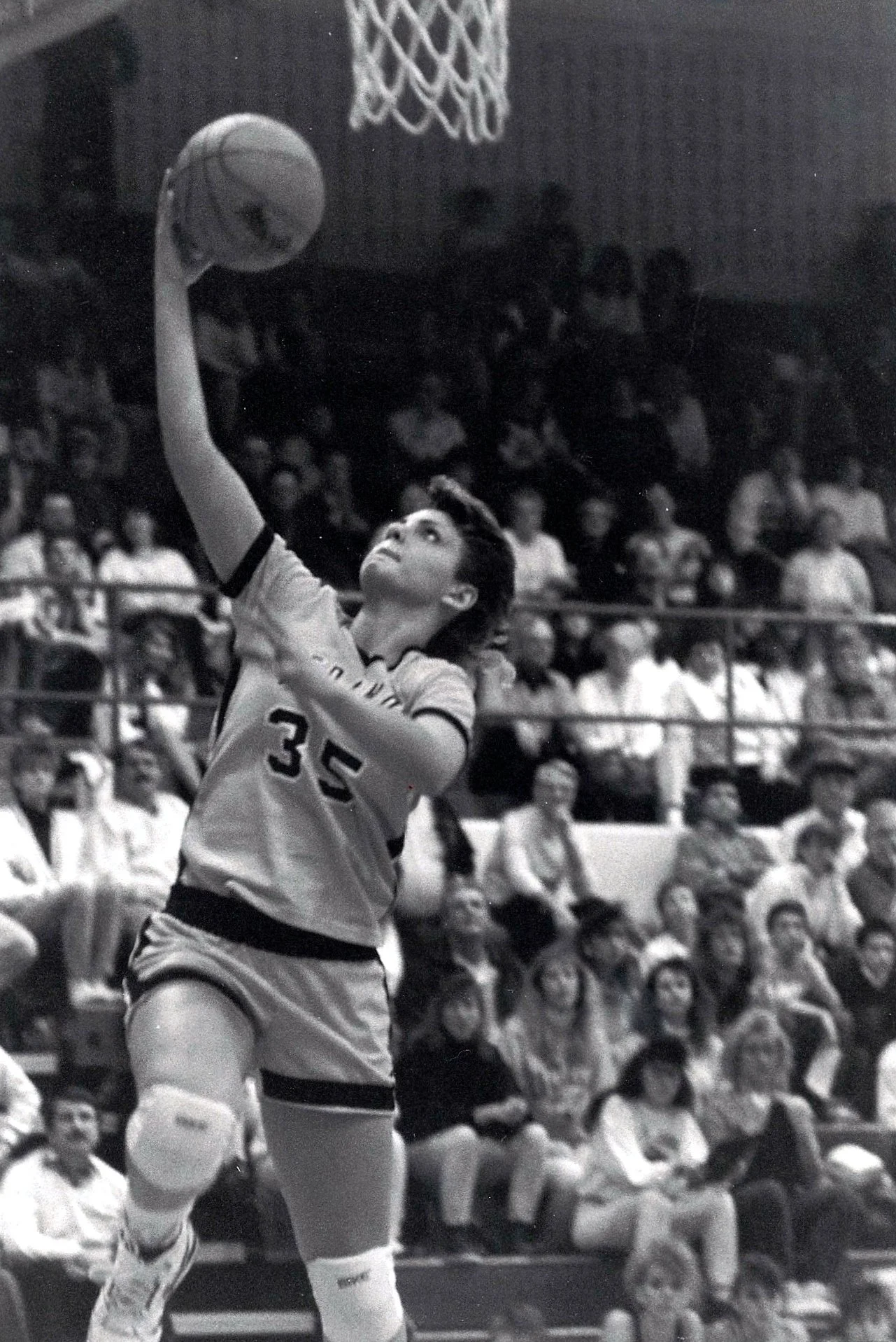 A young woman in a sports uniform with the number 33 on her jersey performing a basketball layup in a gymnasium full of spectators.