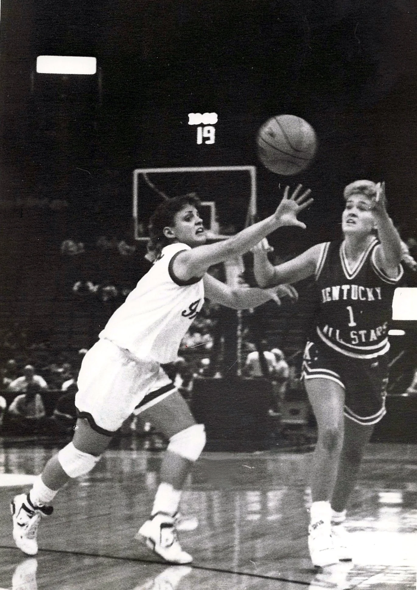 Black and white photo of two female basketball players in action during a game. One player from the University of Kentucky appears to be attempting a shot while the other from the University of Kentucky Wildcats is trying to block it. The crowd can be seen in the background.